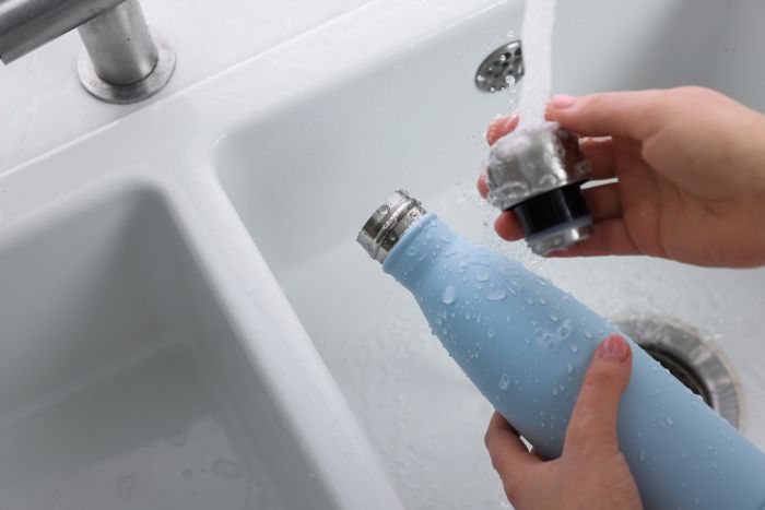 Hände füllen blaue Flasche mit Wasser am Waschbecken. Reinigung in der Küche.