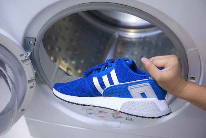 Eine Person, Die Blaue AdidasSchuhe Zur Reinigung In Eine Waschmaschine Legt.