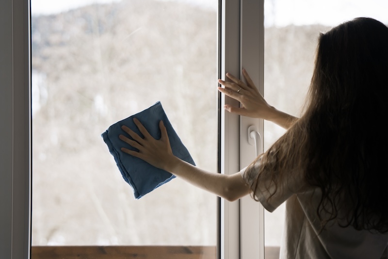 Woman Meticulously Cleans Windowpane Using Blue Cloth With Backdrop Tranquil Snowcovered Environment Visible Through Glass