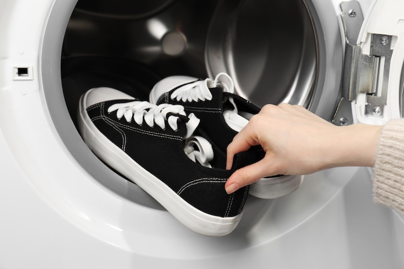 Woman Putting Stylish Sneakers Into Washing Machine Closeup