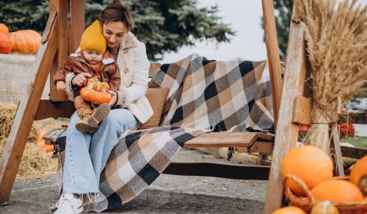 A woman and child enjoy a swing surrounded by pumpkins in a vibrant autumn setting.