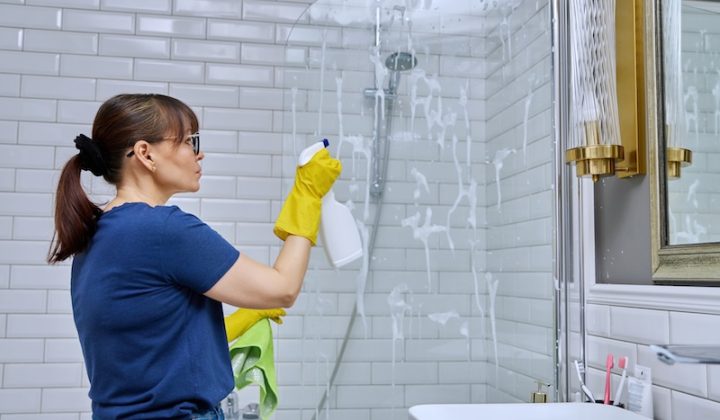 woman cleaning bathroom washing glass shower