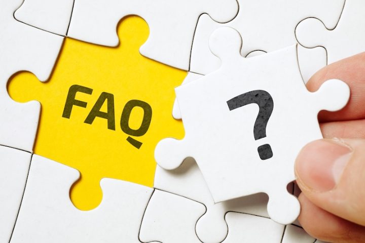 A hand holds a white puzzle piece with a question mark, above a yellow space labeled "FAQ." The image suggests solving questions or uncertainties.