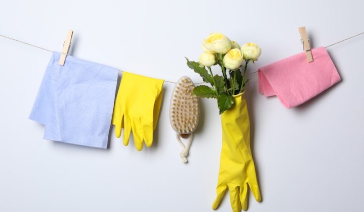 Cleaning items and yellow roses hang on a line. A blue cloth, yellow gloves and brush are clipped between the roses and a pink cloth. Bright and tidy.