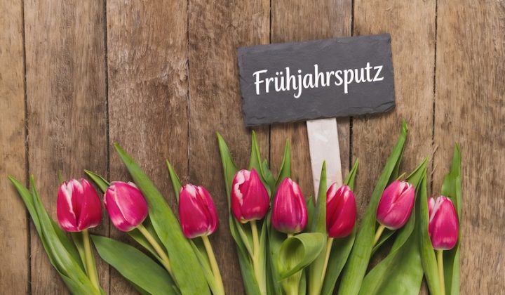 Red Tulips With Green Leaves Line A Rustic Wooden Background. A Small Chalkboard Sign Reads &Quot;Frühjahrsputz,&Quot; Conveying A Fresh, Spring Cleaning Theme.
