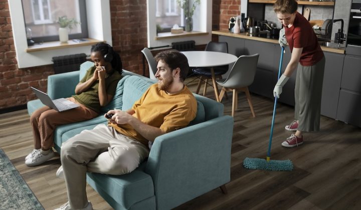 people sitting in a living room with one of them cleaning the floor