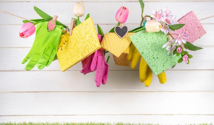 Colorful spring cleaning scene with gloves, sponges, and tulips hanging on a line against a white wooden background. Fresh, cheerful, and organized.