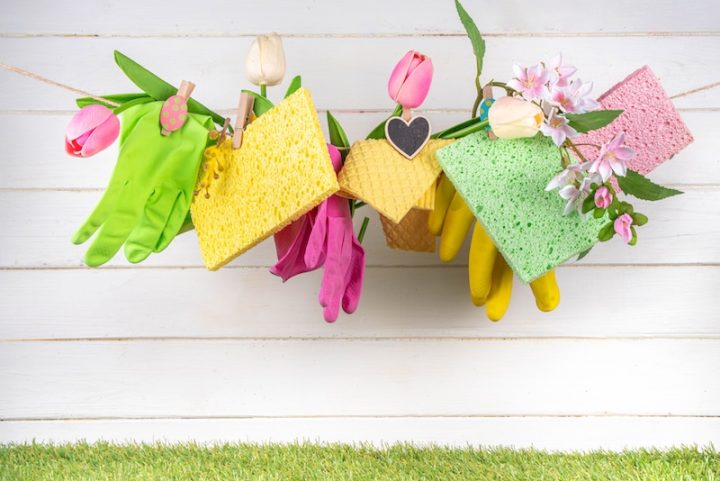 Colorful spring cleaning scene with gloves, sponges, and tulips hanging on a line against a white wooden background. Fresh, cheerful, and organized.