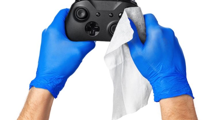 Hands in blue gloves clean a black game controller with a white cloth, set against a plain white background, conveying cleanliness and care.