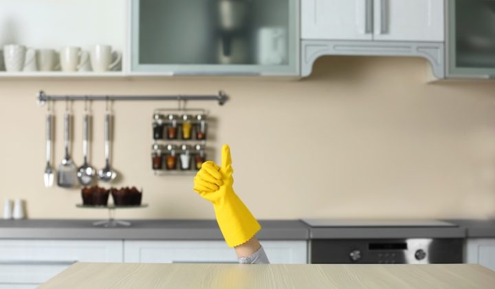 A YellowGloved Hand Gives A ThumbsUp, Emerging From Behind A Kitchen Counter. The Modern Kitchen Has Utensils And Spice Jars On The Wall, Creating A Humorous Tone.