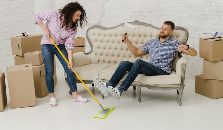 woman mopping floor near resting man in living room full of boxes