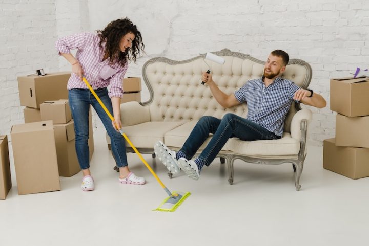 woman mopping floor near resting man in living room full of boxes