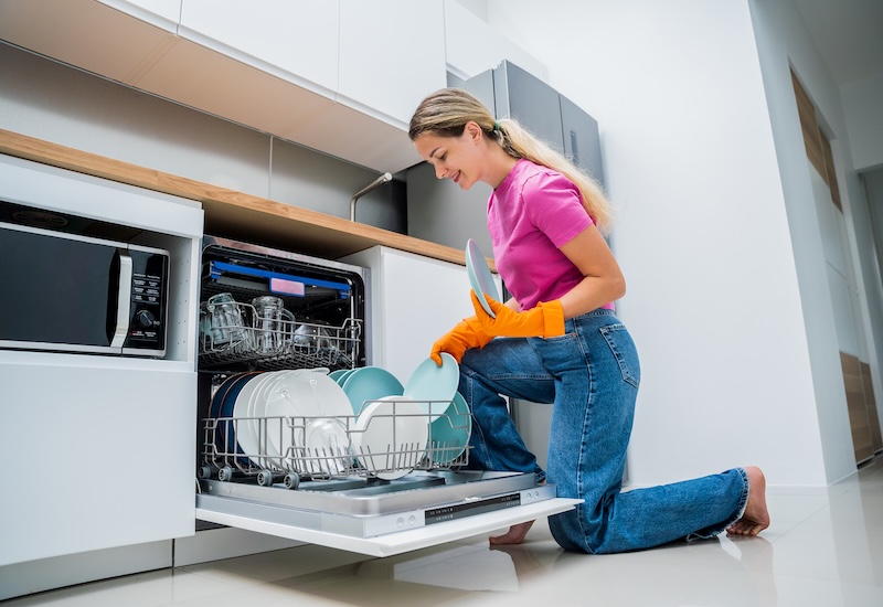 Young Woman Takes Dishes Out Dishwasher Machine